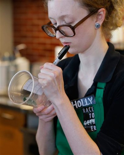 On a Wednesday, March 18, 2015 photo, a barista at a Seattle Starbucks store writes on a cup for an iced drink as she wears a “Race Together” sticker. (AP Photo/Ted S. Warren, File)