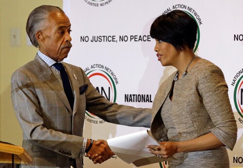 NBC’s Al Sharpton shakes hands with Baltimore Mayor Stephanie Rawlings-Blake as she prepares to speak at a summit to address issues surrounding the death of Freddie Gray and its aftermath at New Shiloh Baptist Church, Thursday, April 30, 2015, in Baltimore. Note the “No Justice, No Peace” slogan behind them. (AP Photo/Patrick Semansky)